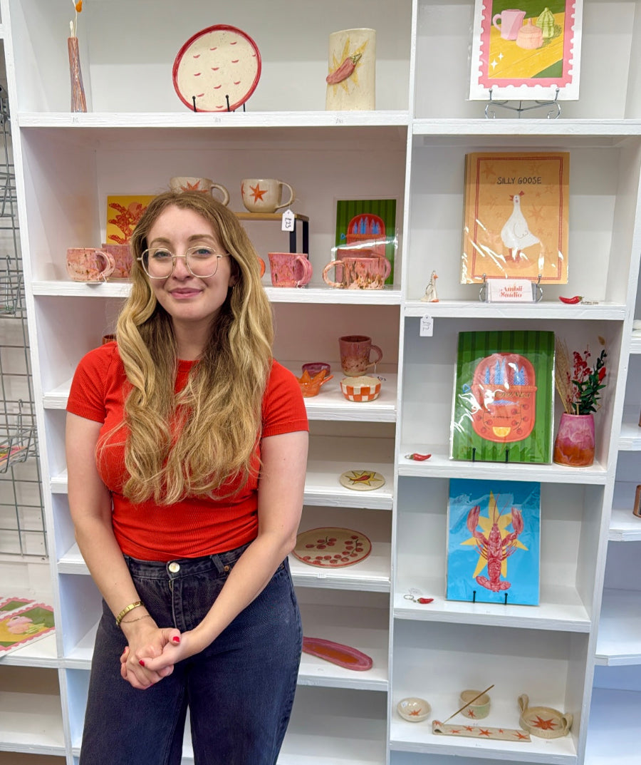 Alice, the owner of Ambii Studios, standing in front of a white bookshelf filled with various decorative items.